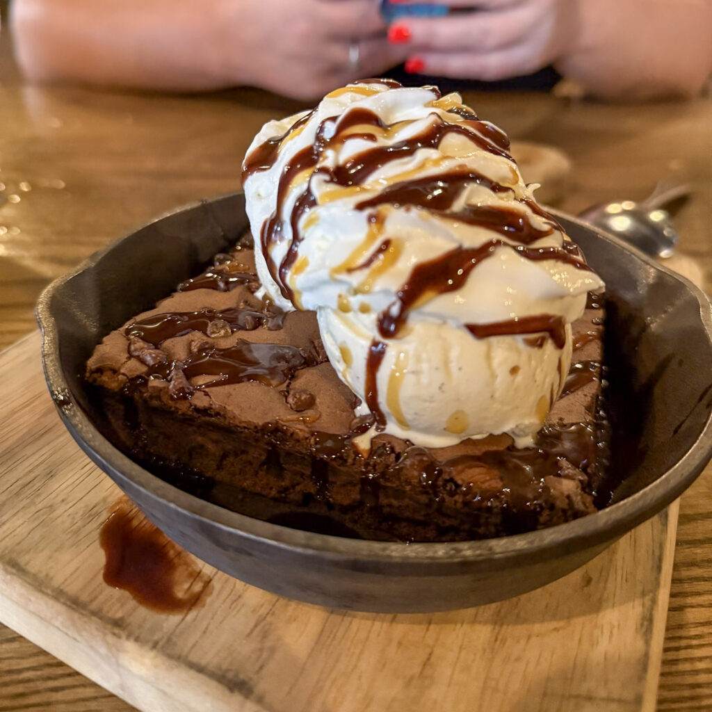 A warm brownie sundae from Westside Social in Grand Rapids, topped with scoops of vanilla ice cream, whipped cream, chocolate sauce, and caramel drizzle.